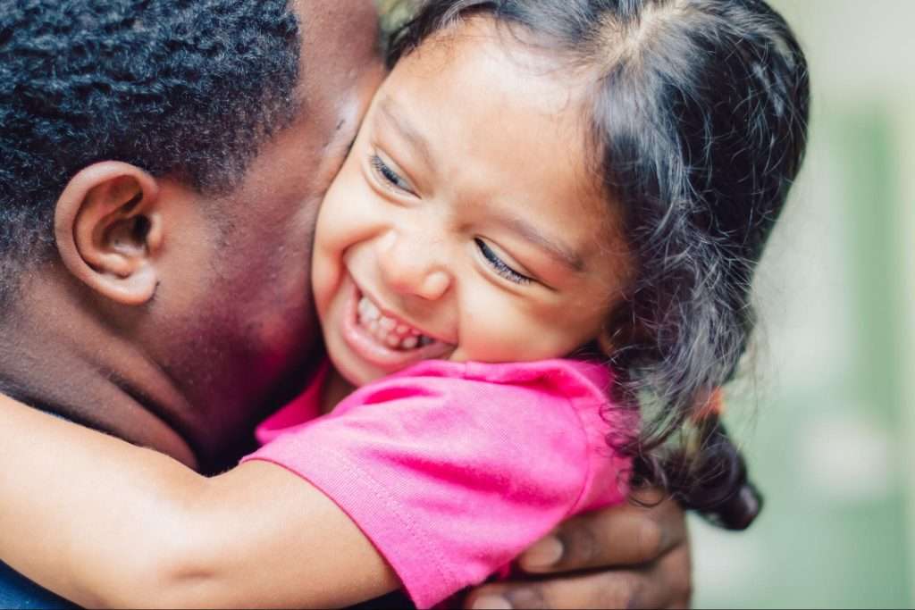 A joyful young girl hugs an adult, representing emotional connection and how to help children through love and support.